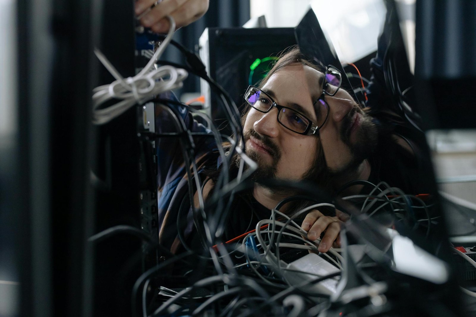 A skilled IT technician organizing tangled cables at his workstation in an office environment.